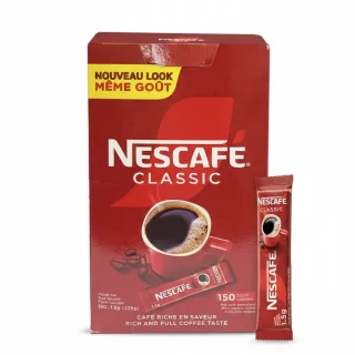 Boîte rouge de sticks Nescafé Classic sur une table en bois dans un marché africain.