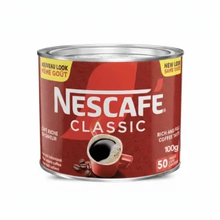Femme d'affaires noire en costume bleu buvant du café devant son ordinateur avec un pot de Nescafé Classic sur son bureau.