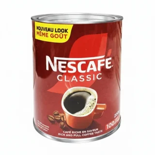 Homme noir en chemise buvant son café avec un pot de Nescafé Classic sur son bureau.